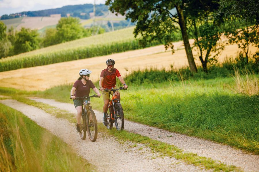 Paar auf E-Bikes radelt über einen Feldweg durch die hügelige Landschaft des Rottals
